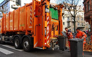 Müllwagen mit Abfalltonnen, die von zwei Mitarbeitern geleert werden