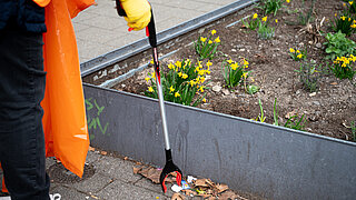 Eine Person greift mithilfe einer Greifzange Müll vom Gehweg.