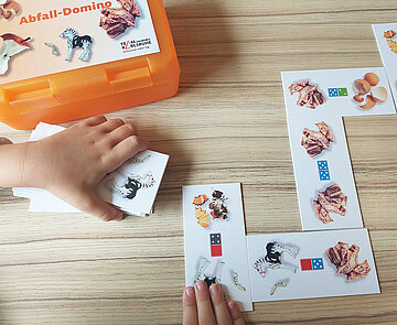 Zwei Kinderhände legen ein Memoryspiel mit Abfallbildern