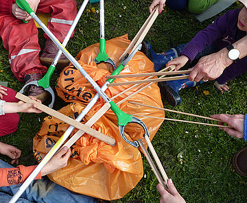 Hände mit Greifzangen über einem Drecksack zum Sammeln von Abfällen