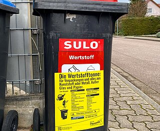 Wertstofftonne mit Gurdulic Aufkleber steht am Straßenrand