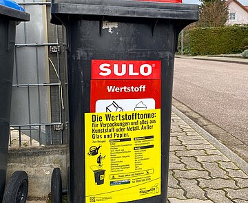 Wertstofftonne mit Gurdulic Aufkleber steht am Straßenrand