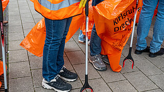 Mehrer Personen stehen mit Greifzange und Müllsack bereit zum Müll aufsammeln.