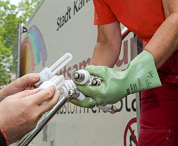 Nahaufnahmer zweier Hände, die Glühbirnen an zwei andere Hände übergibt