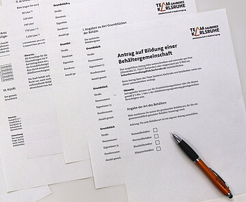 Mehrere Formularevordrucke liegen auf einem Tisch mit einem Kugelschriber darüber