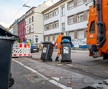 Ein Müllarbeiter rollt zwei Tonnen auf die Straße zum Müllfahrzeug.