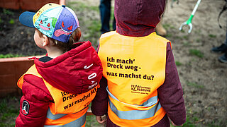 Zwei Kinder tragen eine orangefarbene Weste mit dem Aufdruck "Ich mach Dreck weg – mach mit"