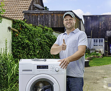 Bild eines zufriedeneMannes, der seine alte Waschmaschine zur Entsorgung durch das Team Sauberes Karlsruhe an der Straße bereit stellt